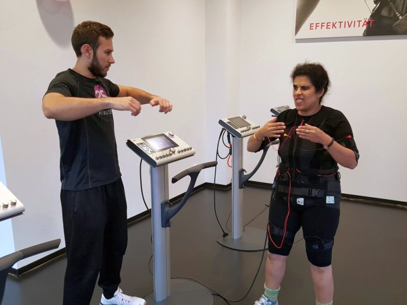 Lydia mit angeschlossenem EMS-Anzug, neben mir steht Yves und erklärt mir eine Übung.