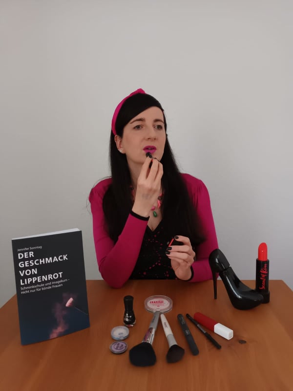 Jennifer Sonntag an einem Tisch mit Schminkutensilien und ihrem Buch Der Geschmack von Lippenrot